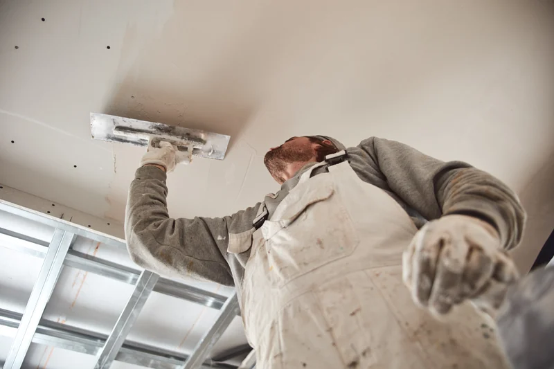 Worker skimming a ceiling below an exposed metal grid