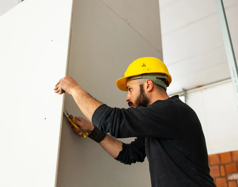 Worker measuring and scoring a drywall sheet before cutting